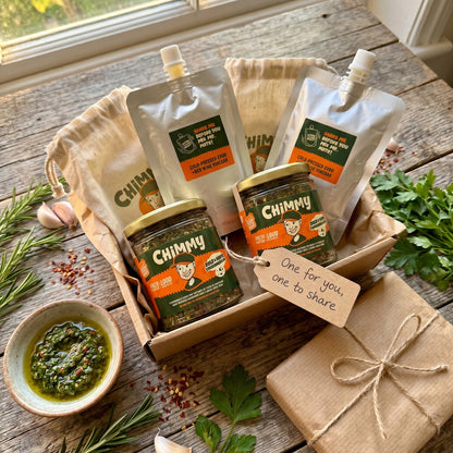 Double Drizzle gift duo — two Chimmy chimichurri kits (two herb jars and two cold-pressed EVOO + red wine vinegar pouches) in a kraft gift box with a tag reading One for you, one to share, fresh rosemary, parsley, garlic and a bowl of mixed chimichurri