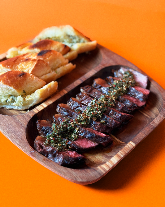 Sliced grilled steak drizzled with Chimmy chimichurri sauce, served on a wooden board with toasted bread